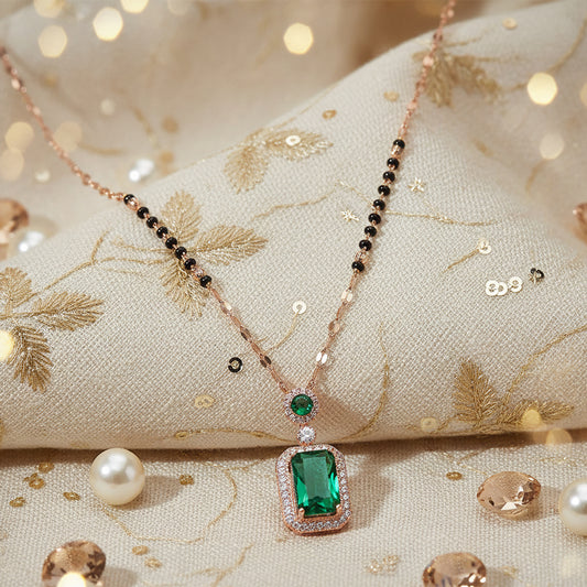 Gold mangalsutra with green solitaire pendant displayed on an embroidered fabric background