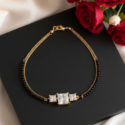 Elegant black beads mangalsutra gold bracelet featuring three square sparkling stones, displayed on a black box with red roses in the background.
