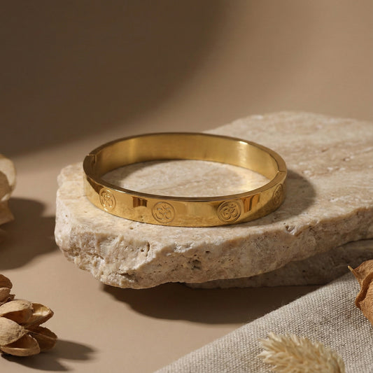 A luxury hand bracelet for men with a polished gold finish resting on a natural stone.