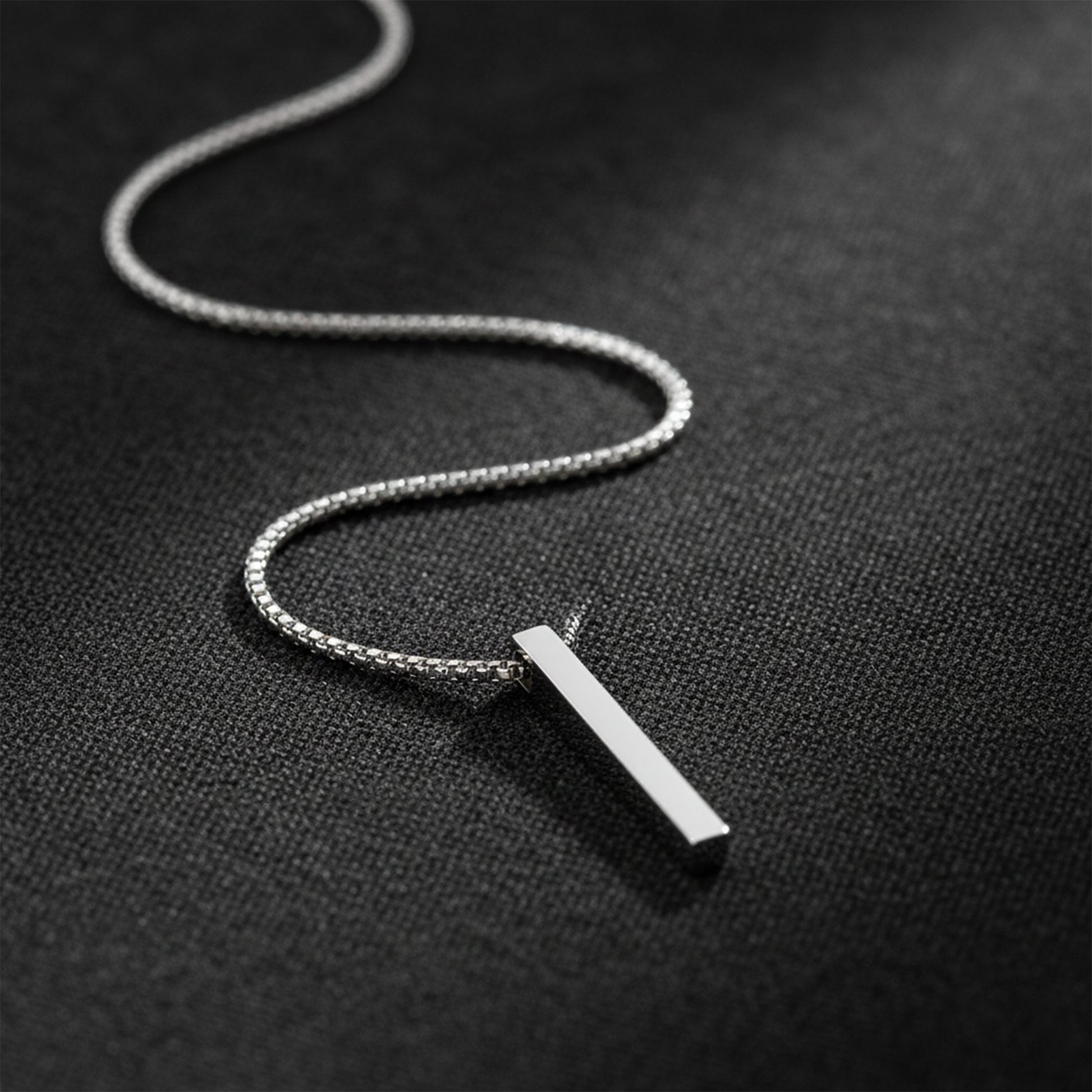 Men’s silver chain necklace with a sleek bar pendant on a dark textured background