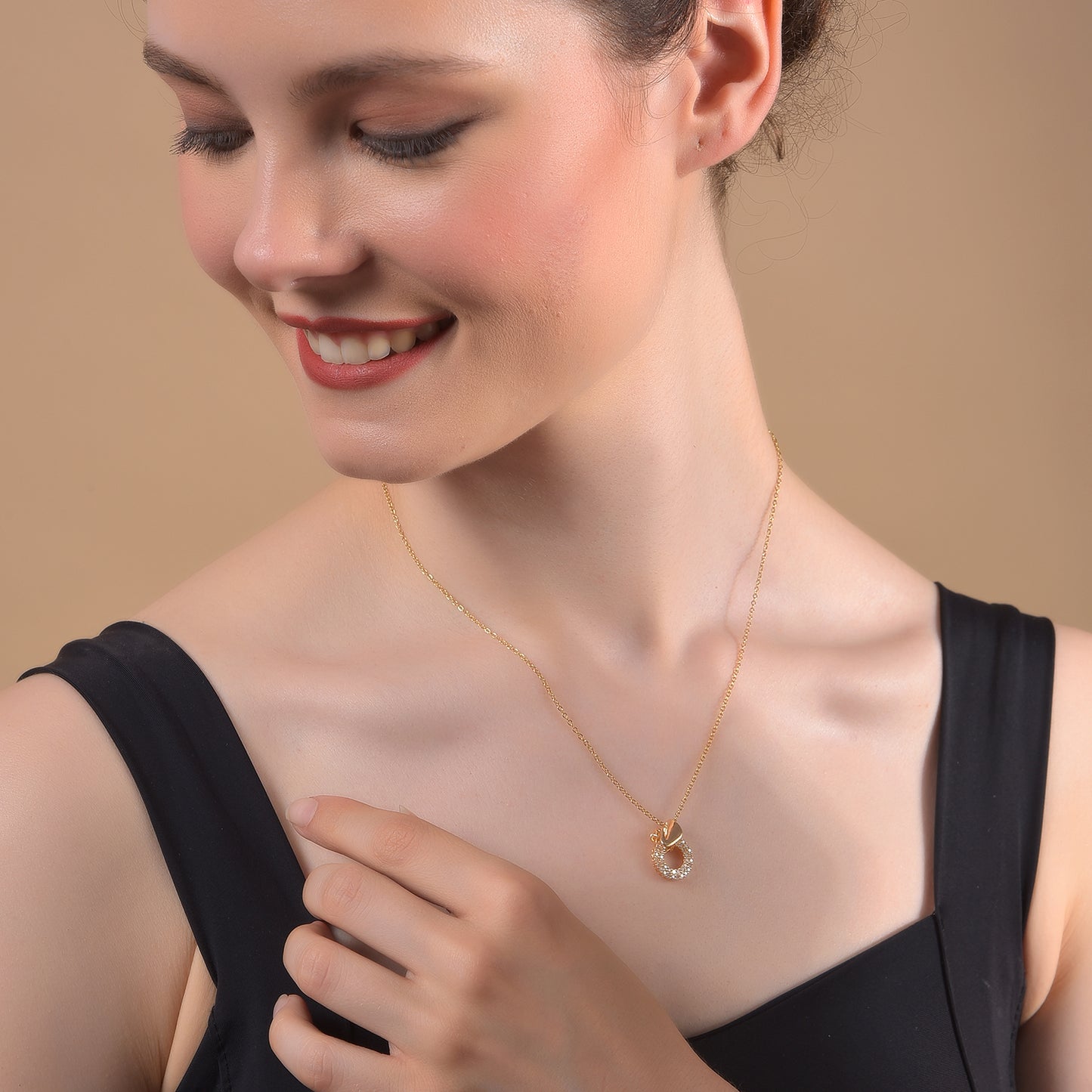 Close-up of a smiling woman wearing a dainty gold necklace for women featuring a small, sparkling circular pendant with inset crystals against a neutral background.