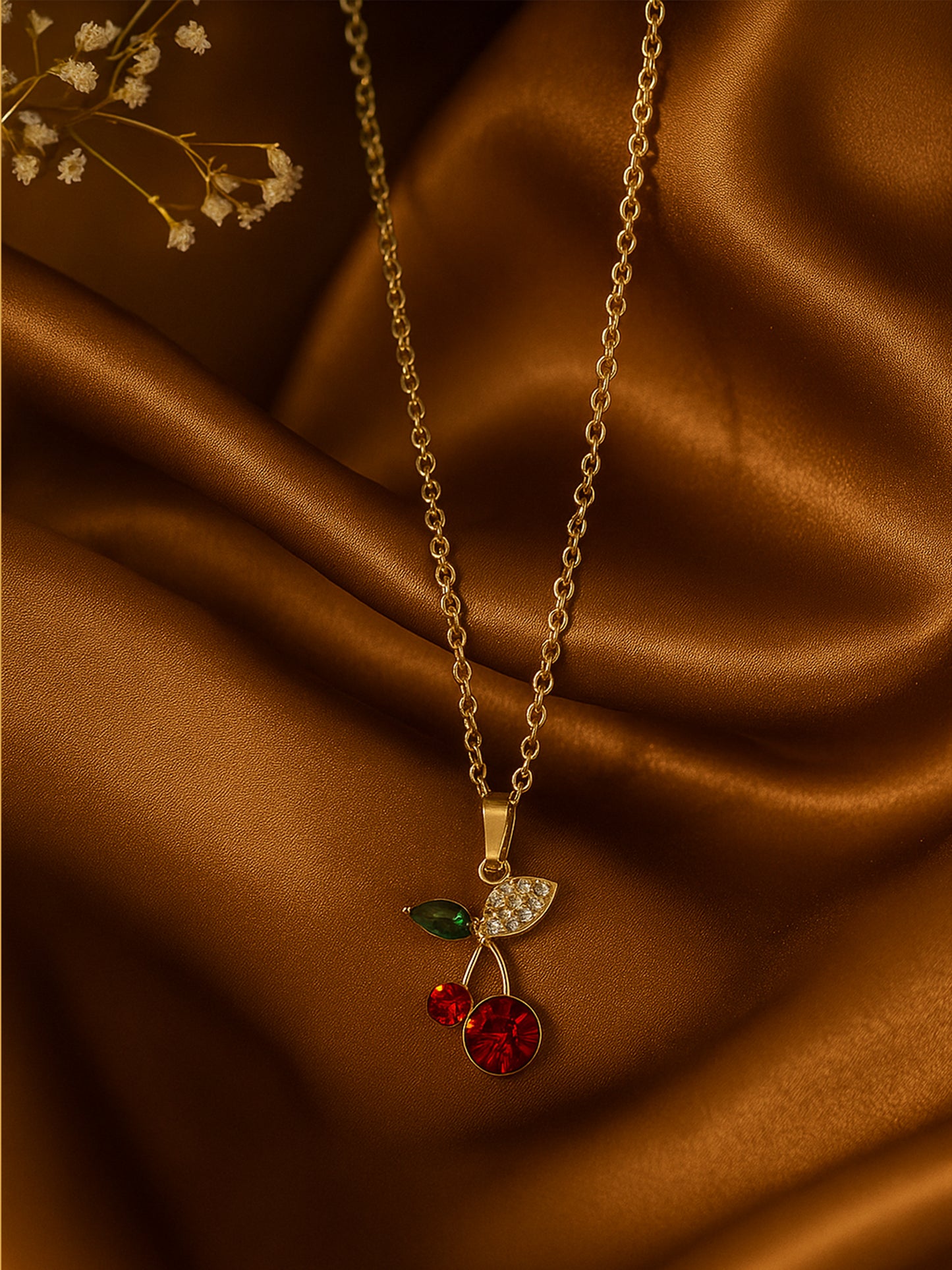 Gold chain with pendant featuring a crystal cherry design with red and green stones on a brown silk background