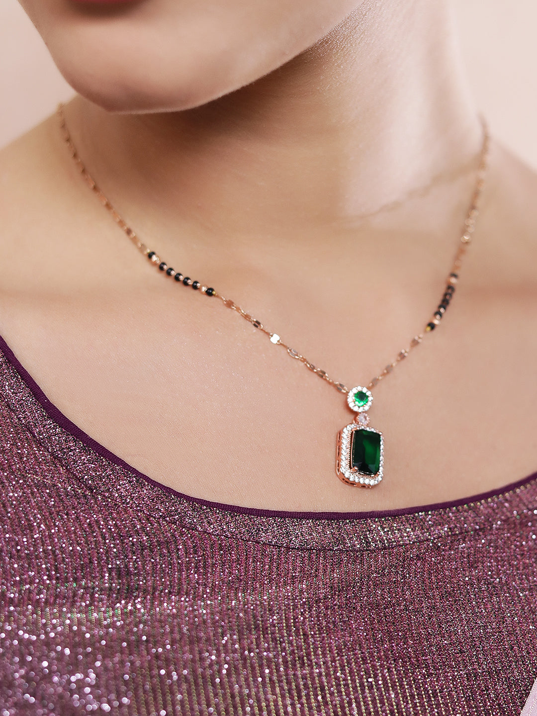 Daily wear mangalsutra design in gold with an emerald pendant, shown in a close-up on a model