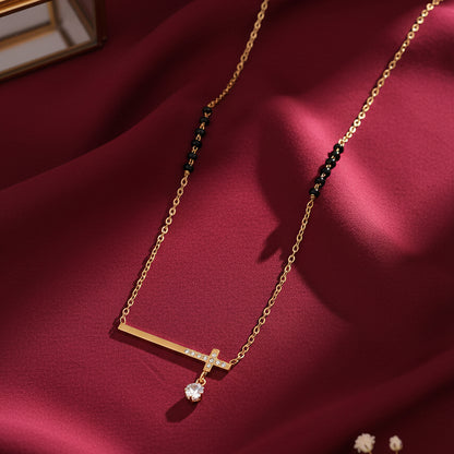 Gold mangalsutra with minimal bar pendant, solitaire drop, and black beads on a maroon fabric background