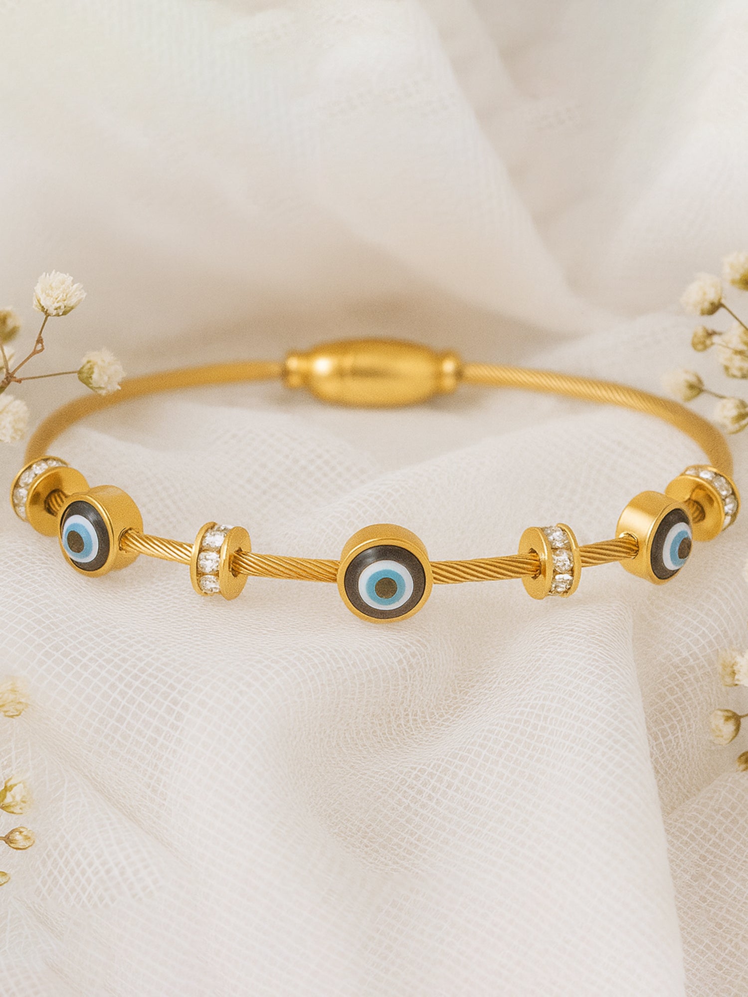 Gold evil eye bracelet for women for daily wear displayed on soft white fabric with flowers.