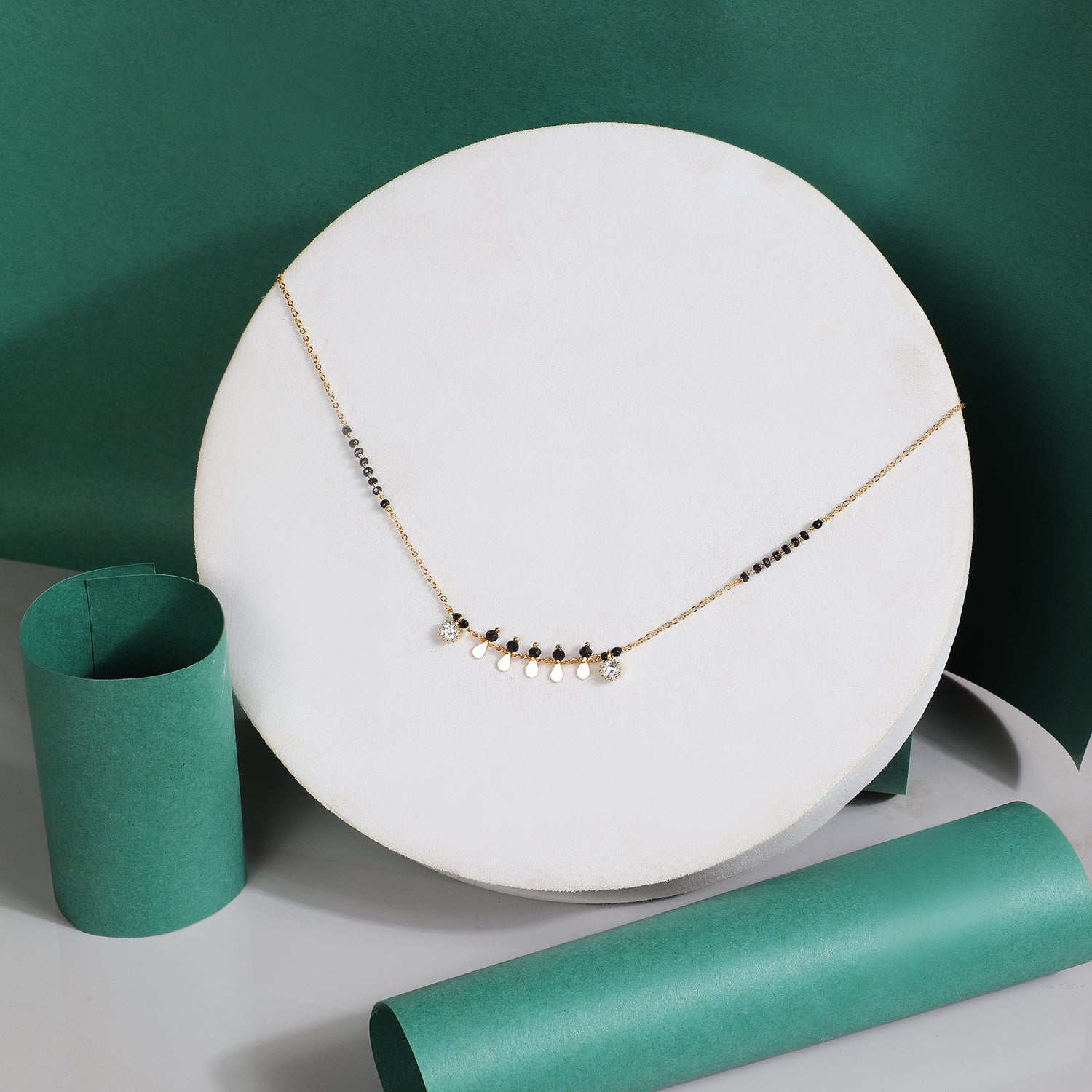 Fancy traditional mangalsutra design with gold chain, black beads, and small gold charm drops displayed on a white stand