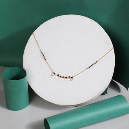 Fancy traditional mangalsutra design with gold chain, black beads, and small gold charm drops displayed on a white stand