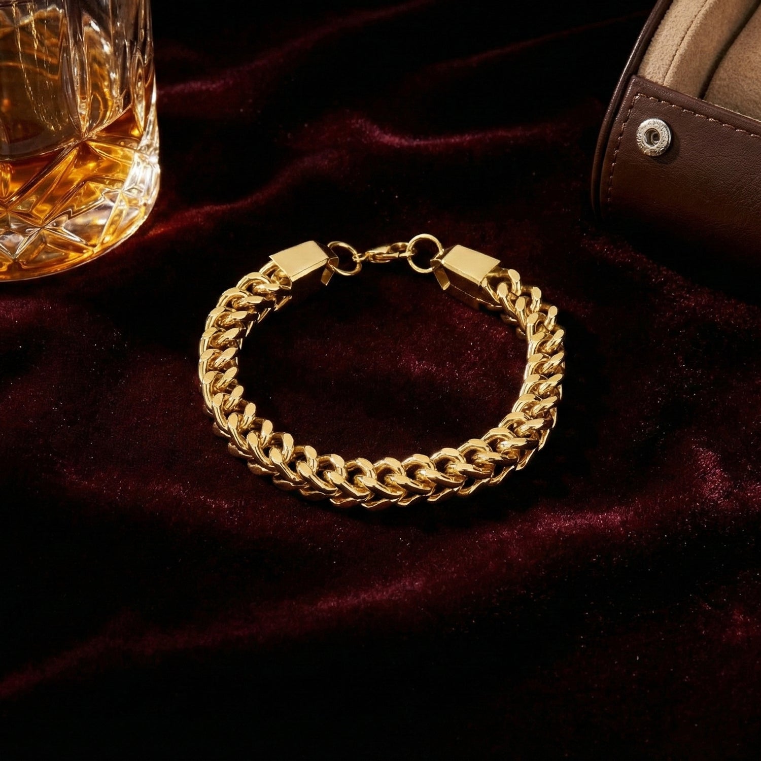 Elegant gold bracelet for men displayed on a luxury velvet surface next to a glass.
