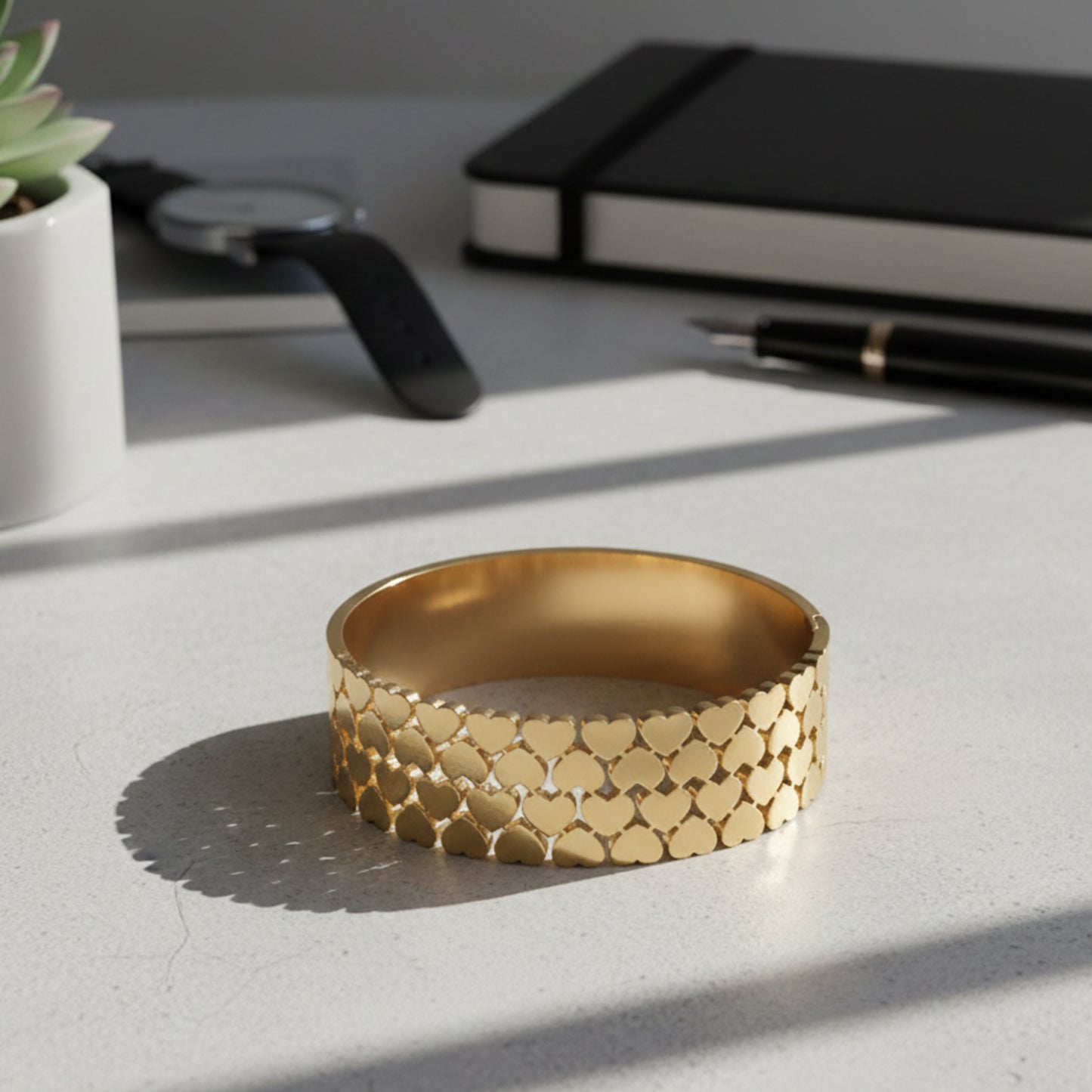 A gold bracelet for women featuring a unique layered heart design on a bright office desk.