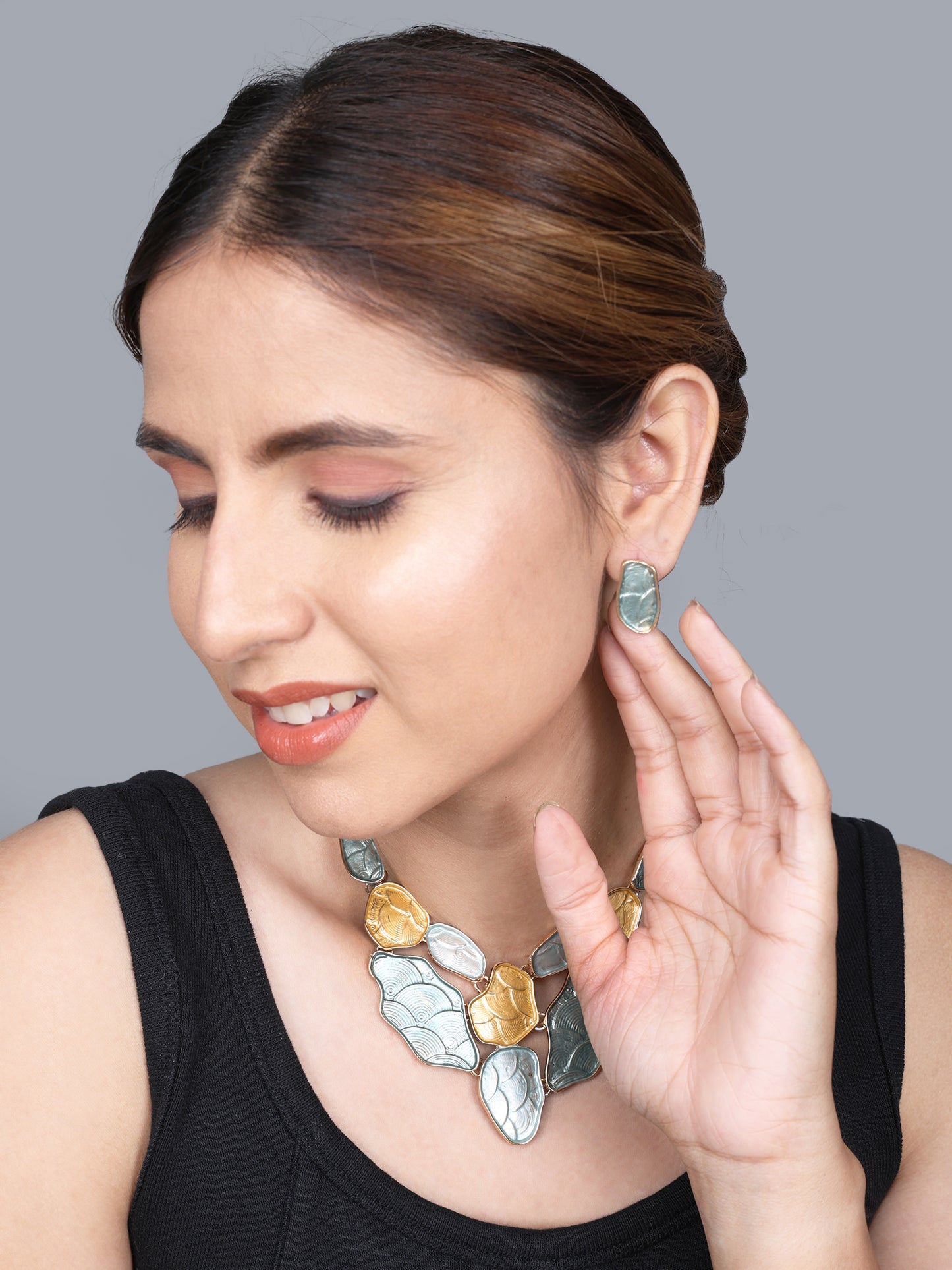 Close up of a gold necklace and earring set featuring unique blue and gold abstract patterns.