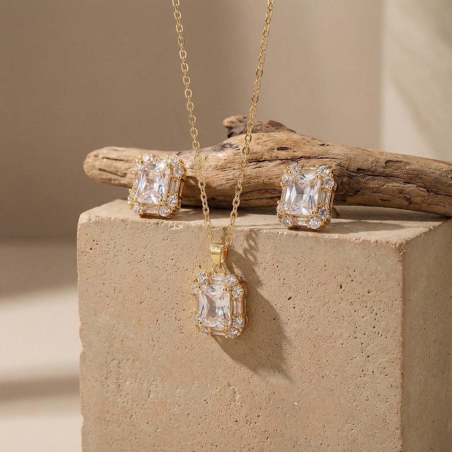 A complete gold necklace and earring set with matching rectangular crystal pendants displayed on a rustic stone background.