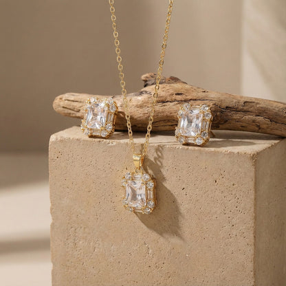 A complete gold necklace and earring set with matching rectangular crystal pendants displayed on a rustic stone background.