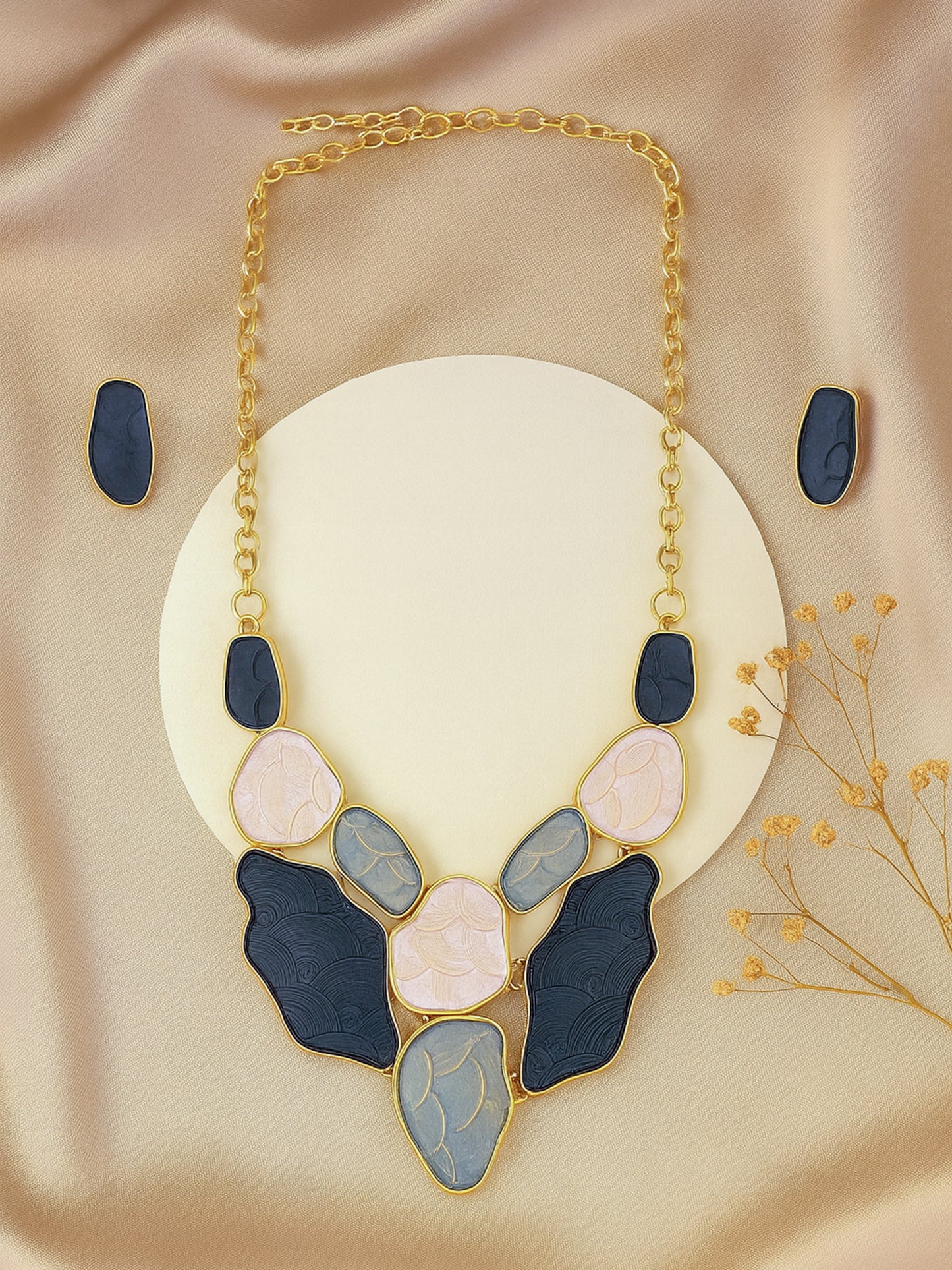 A stunning gold necklace and earring set with artistic enamel stone inlays displayed on a silk background.