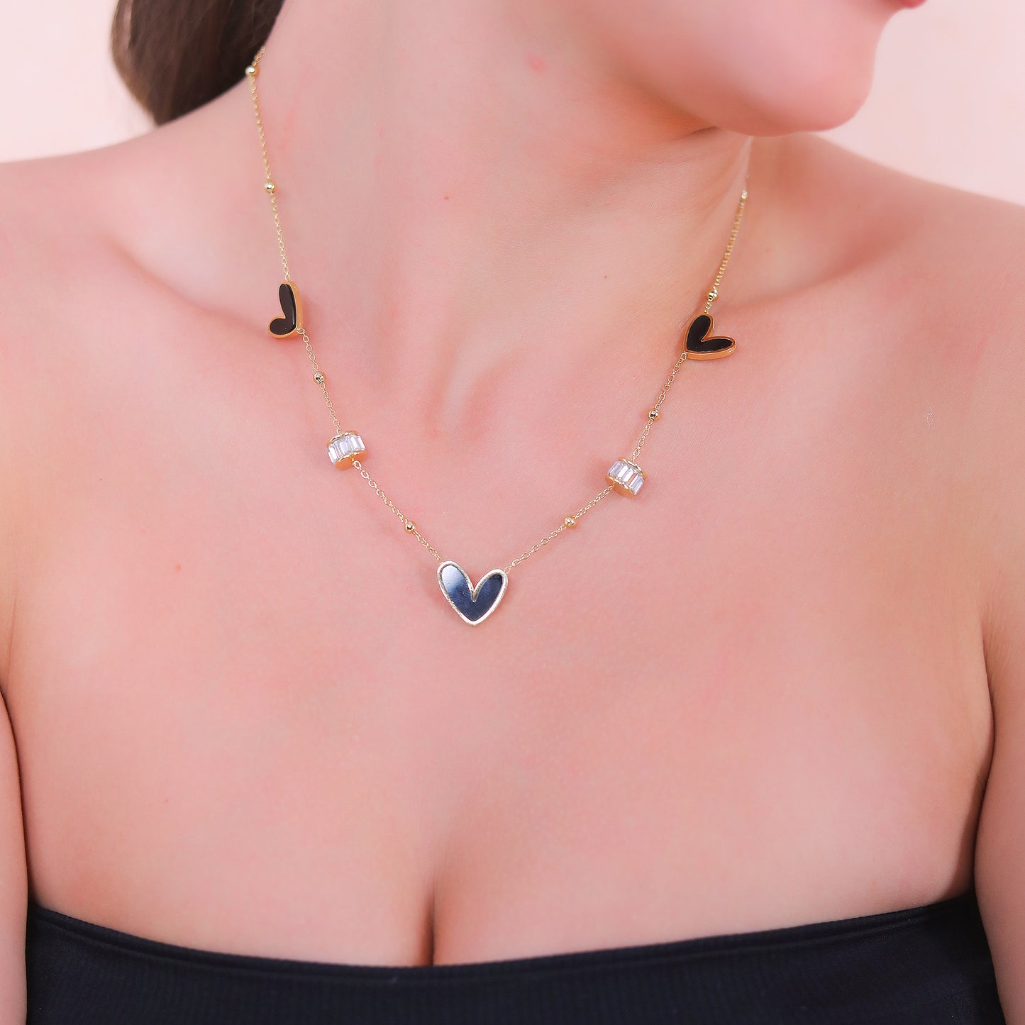 Modern gold necklace design for women featuring black enamel hearts and baguette crystal accents.
