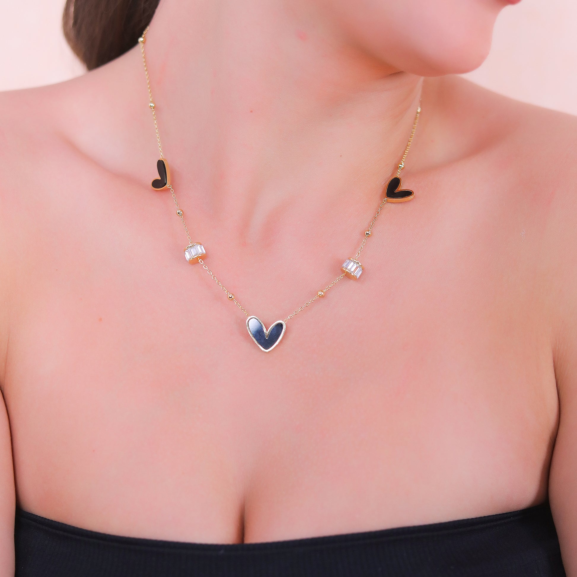 Modern gold necklace design for women featuring black enamel hearts and baguette crystal accents.