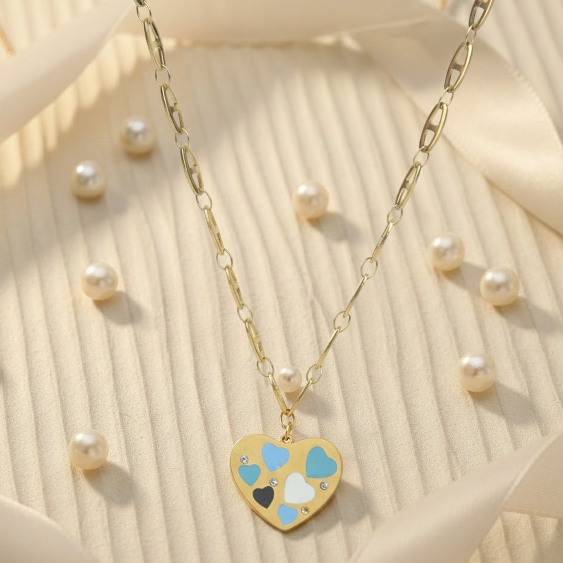 Aesthetic gold necklace for women surrounded by pearls, featuring a heart pendant with blue, white, and black enamel.