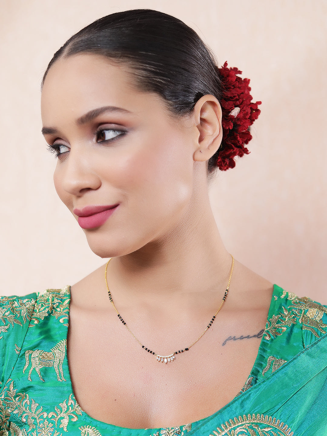 Fancy short mangalsutra design with gold chain, black beads, and a CZ leaf pendant worn by a woman in a green embroidered saree