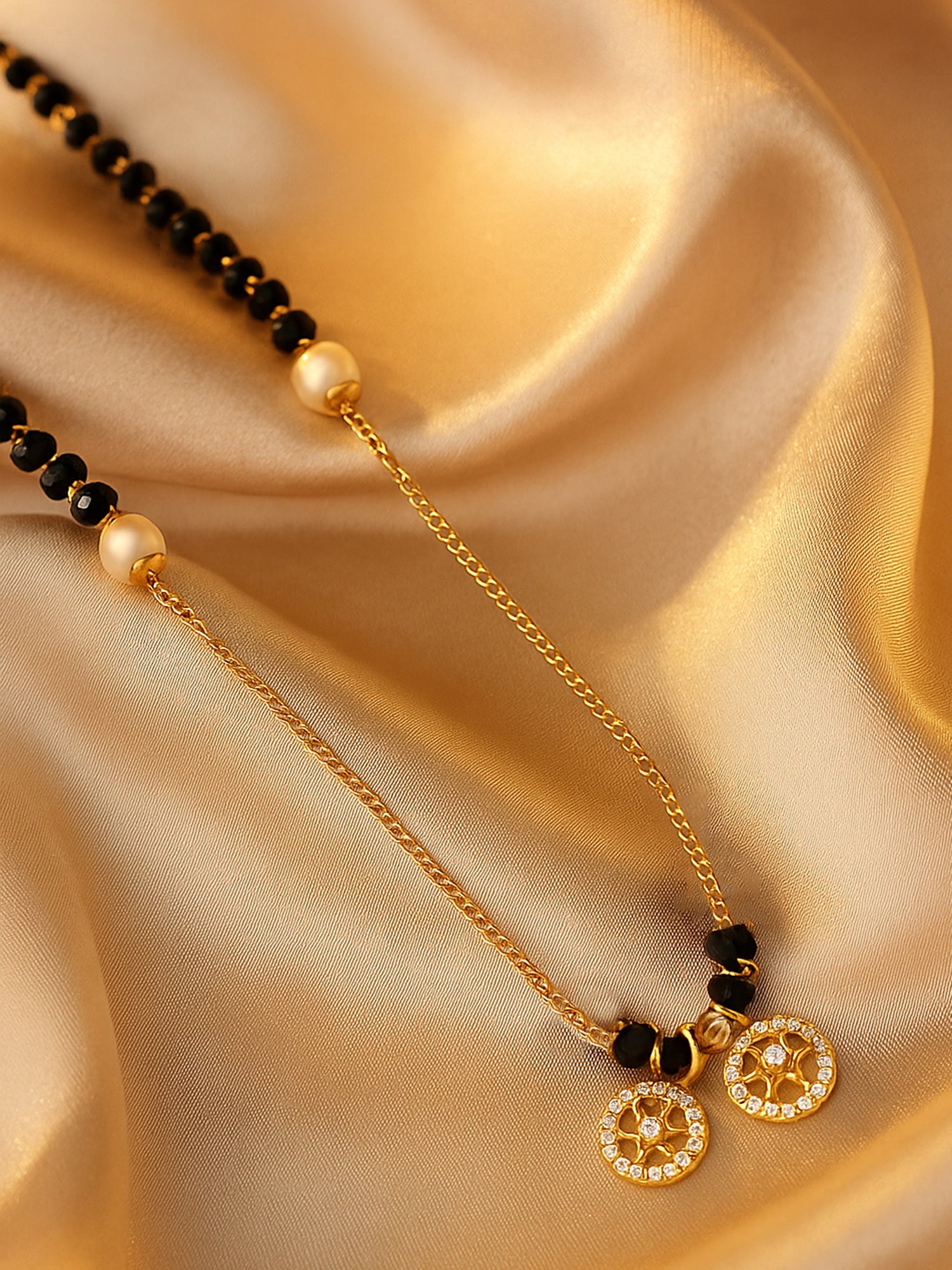 Close-up of black beads mangalsutra gold, featuring two circular wheel pendants on a silky gold background