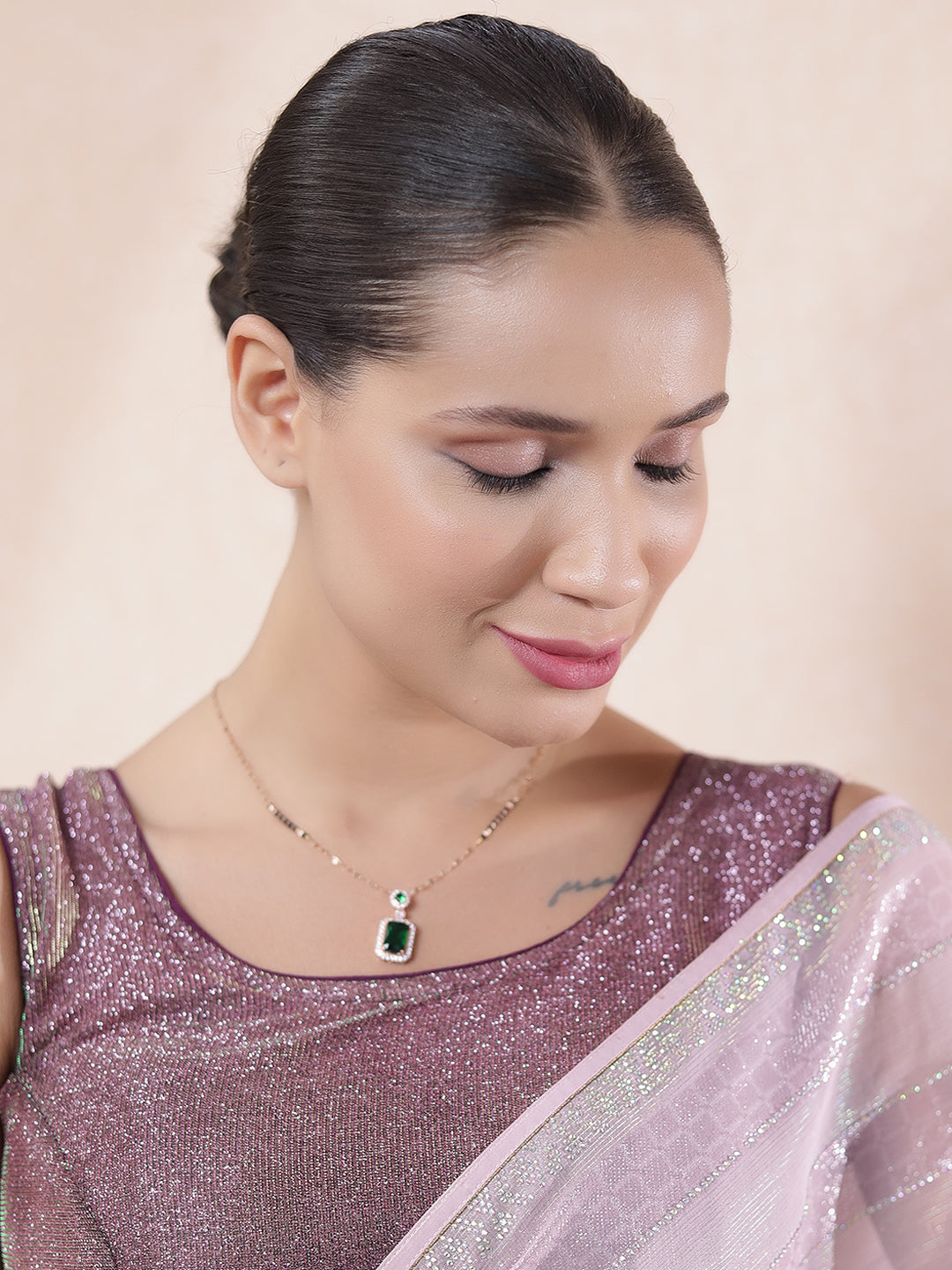 Model wearing the latest mangalsutra design featuring a gold chain with an emerald pendant, styled with a shimmer saree