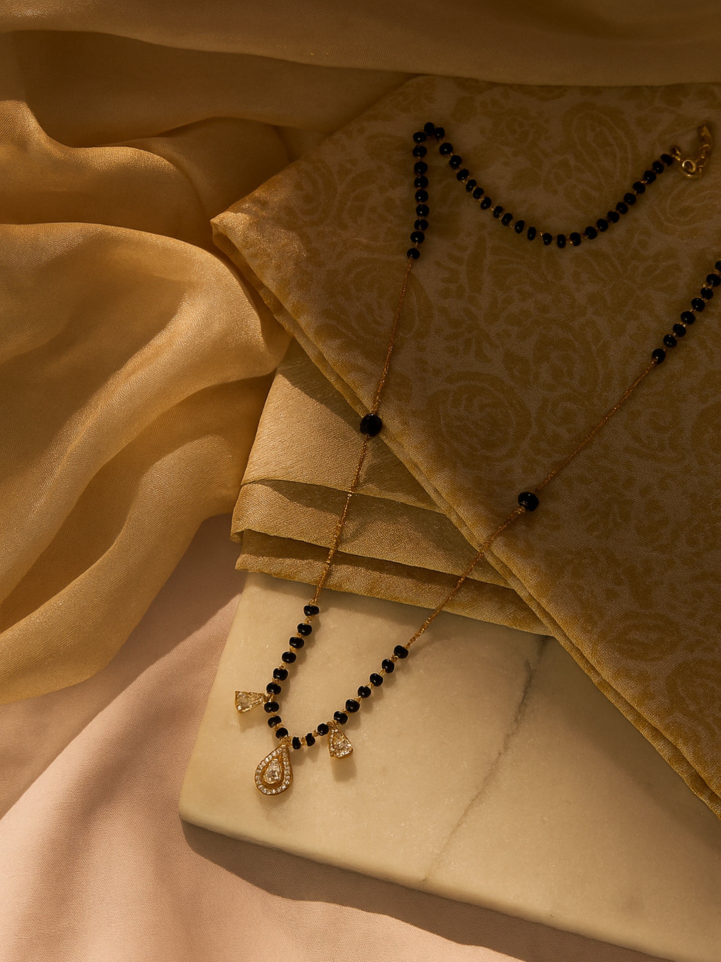Black beads mangalsutra gold featuring delicate gold chain and teardrop crystal pendant on fabric background