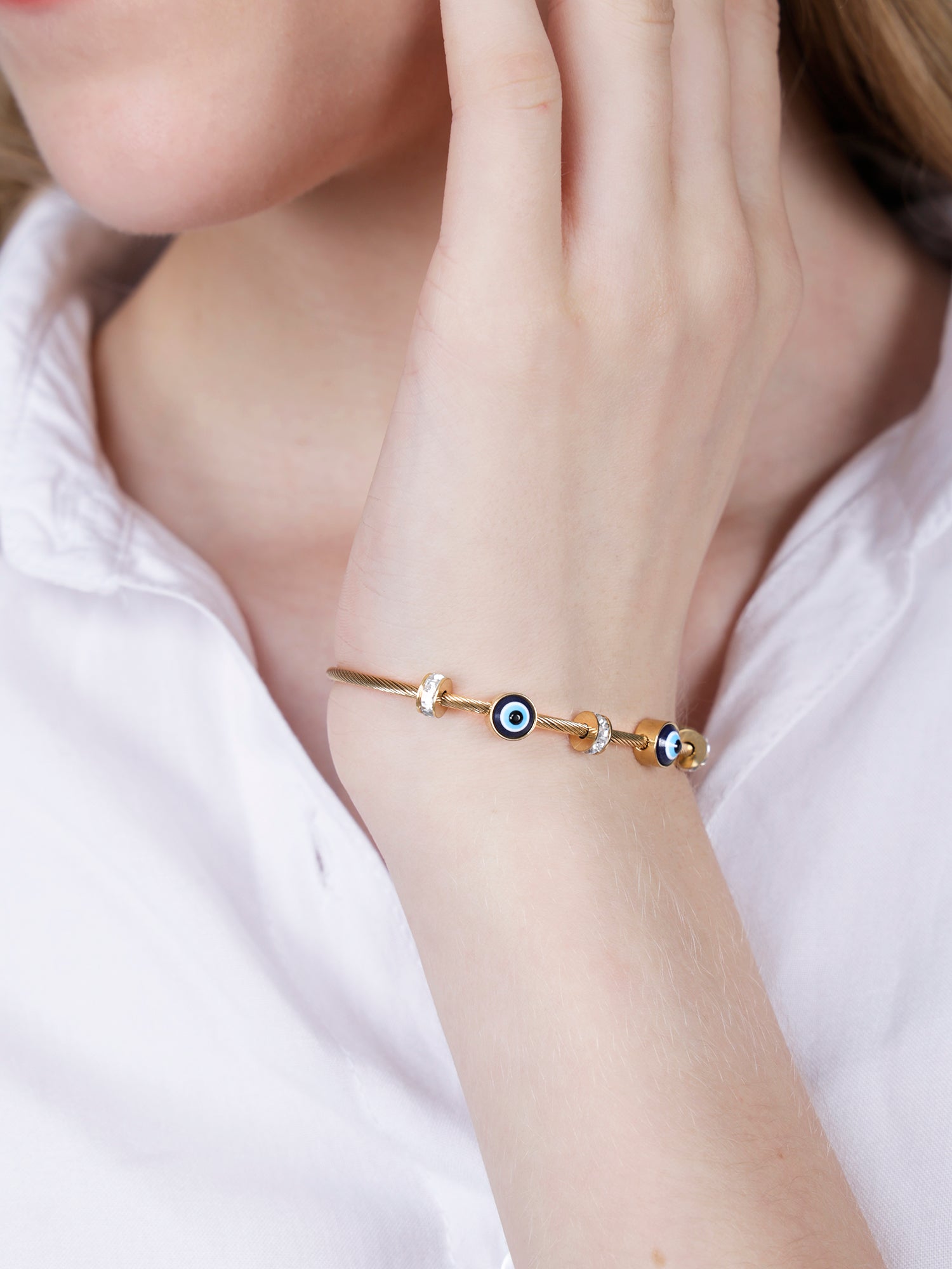 Close up of a gold plated hand bracelet for women worn on a wrist with a white shirt.