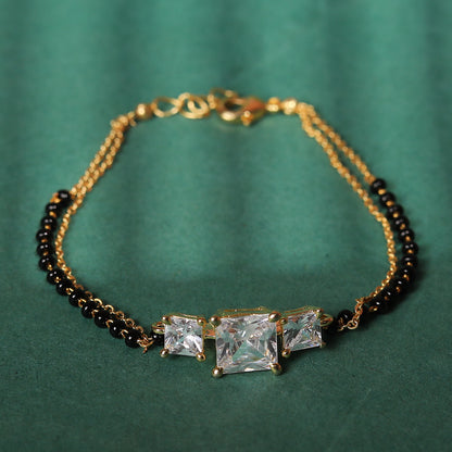 Elegant ladies bracelet gold mangalsutra design featuring dual black-bead chains and three sparkling stone settings on a green background.