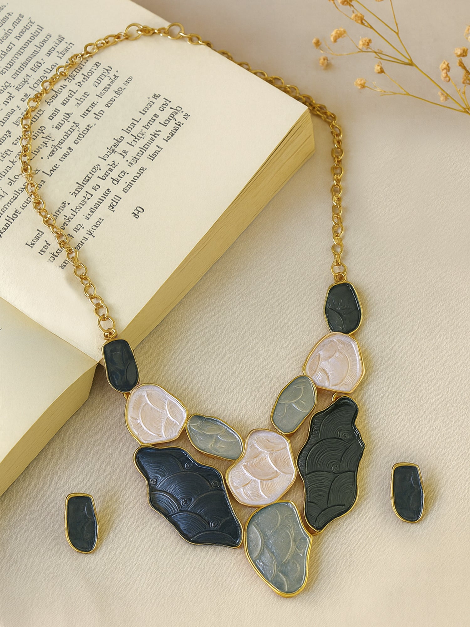 One of the latest gold necklace designs featuring organic-shaped stones arranged in a bib style on a textured cream surface.