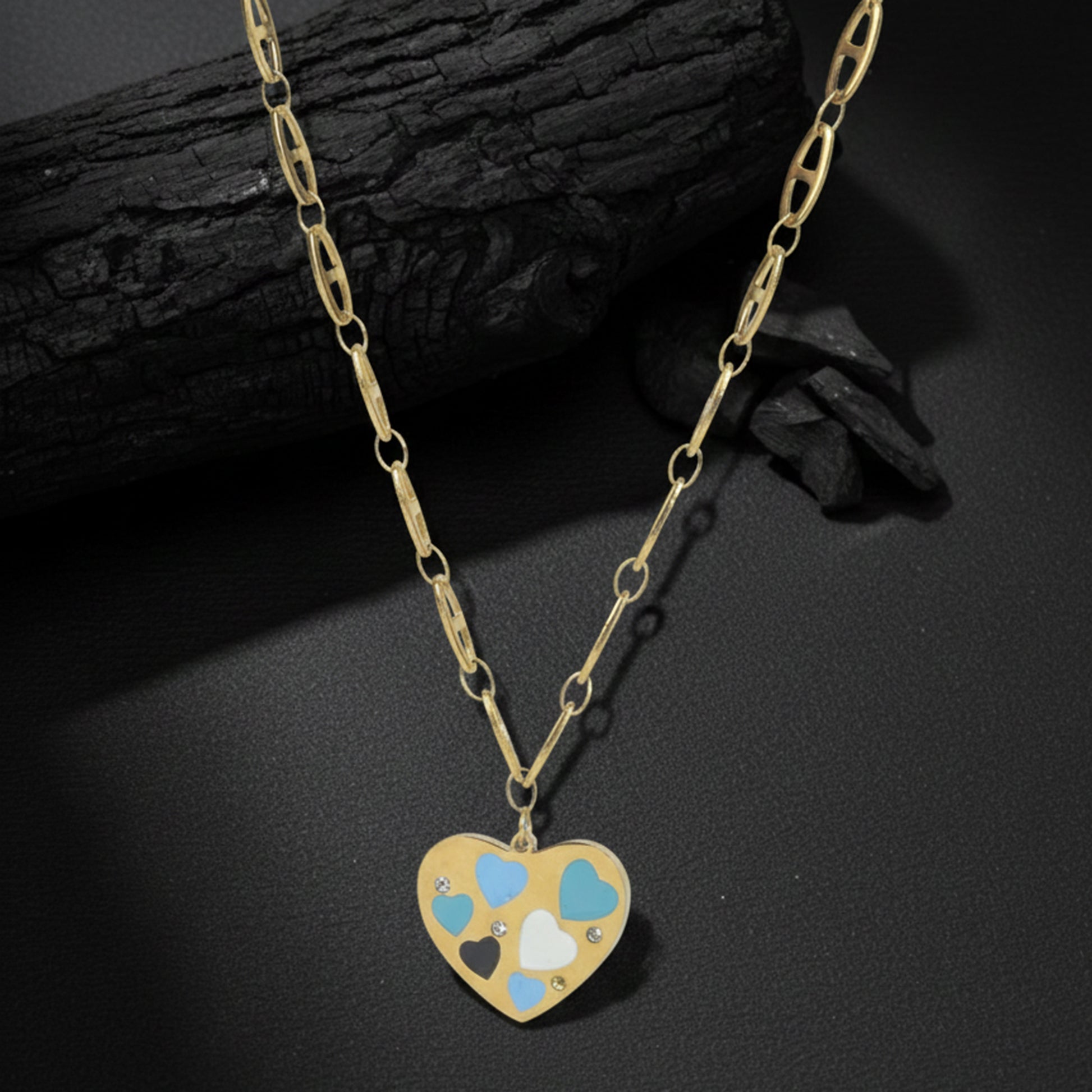 Light weight gold necklace with a decorative heart charm and small crystals, placed on a textured charcoal surface.