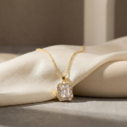 A light weight gold necklace featuring a dainty gold chain and a rectangular crystal pendant resting on soft cream fabric.