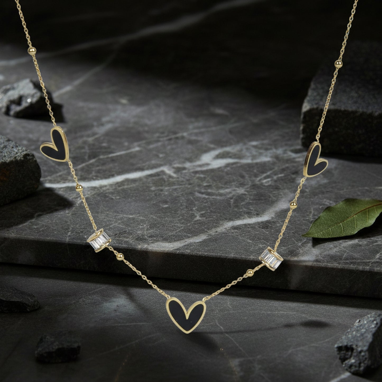 Light weight gold necklace with black heart inlays and crystals resting on dark marble stone.