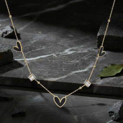 Light weight gold necklace with black heart inlays and crystals resting on dark marble stone.