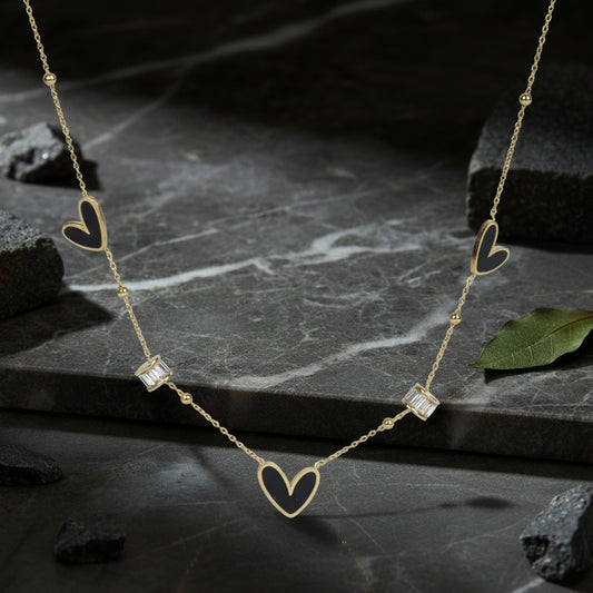 Light weight gold necklace with black heart inlays and crystals resting on dark marble stone.