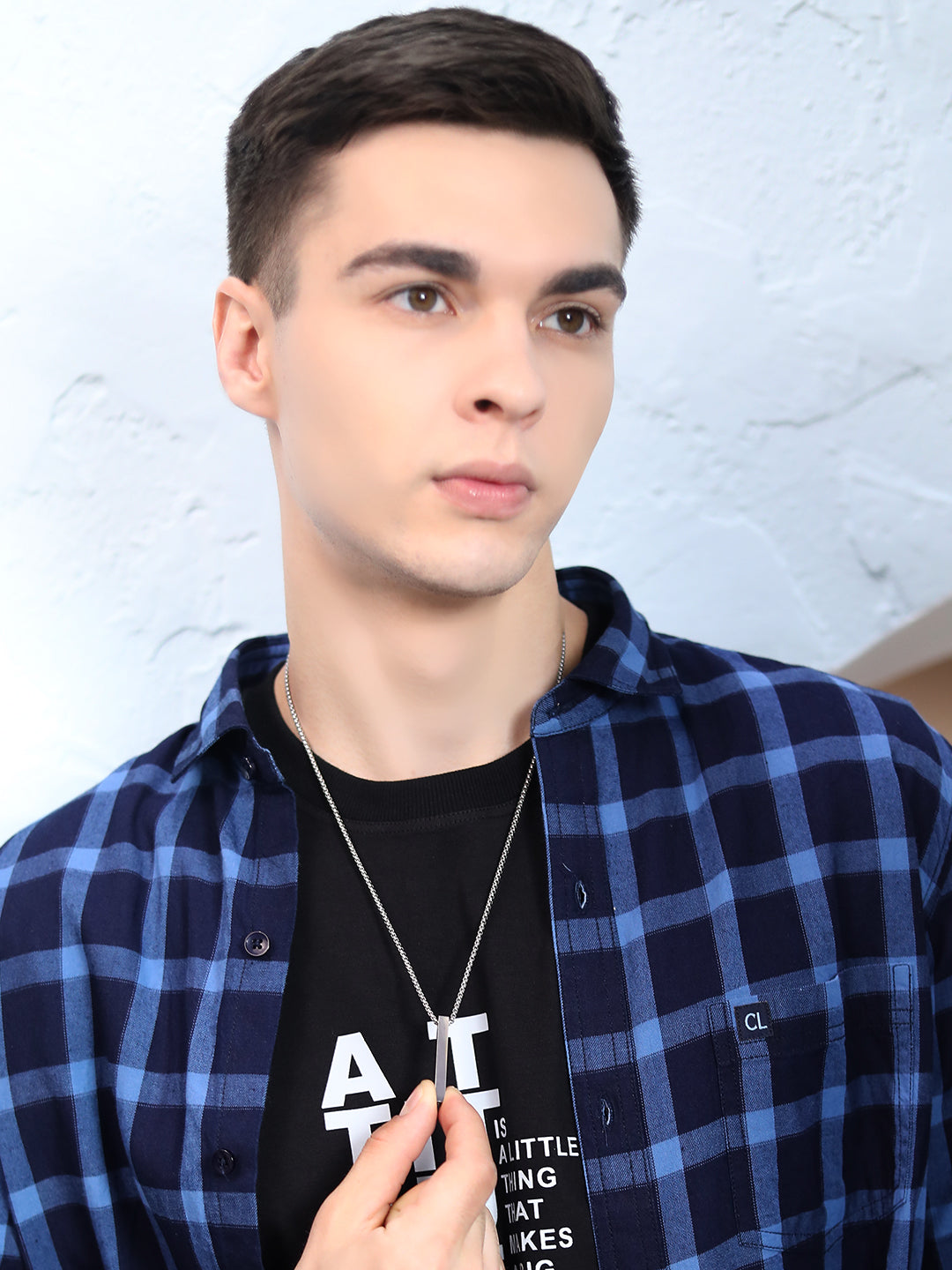 Man wearing a mens silver pendant on a thin chain, holding the bar pendant.