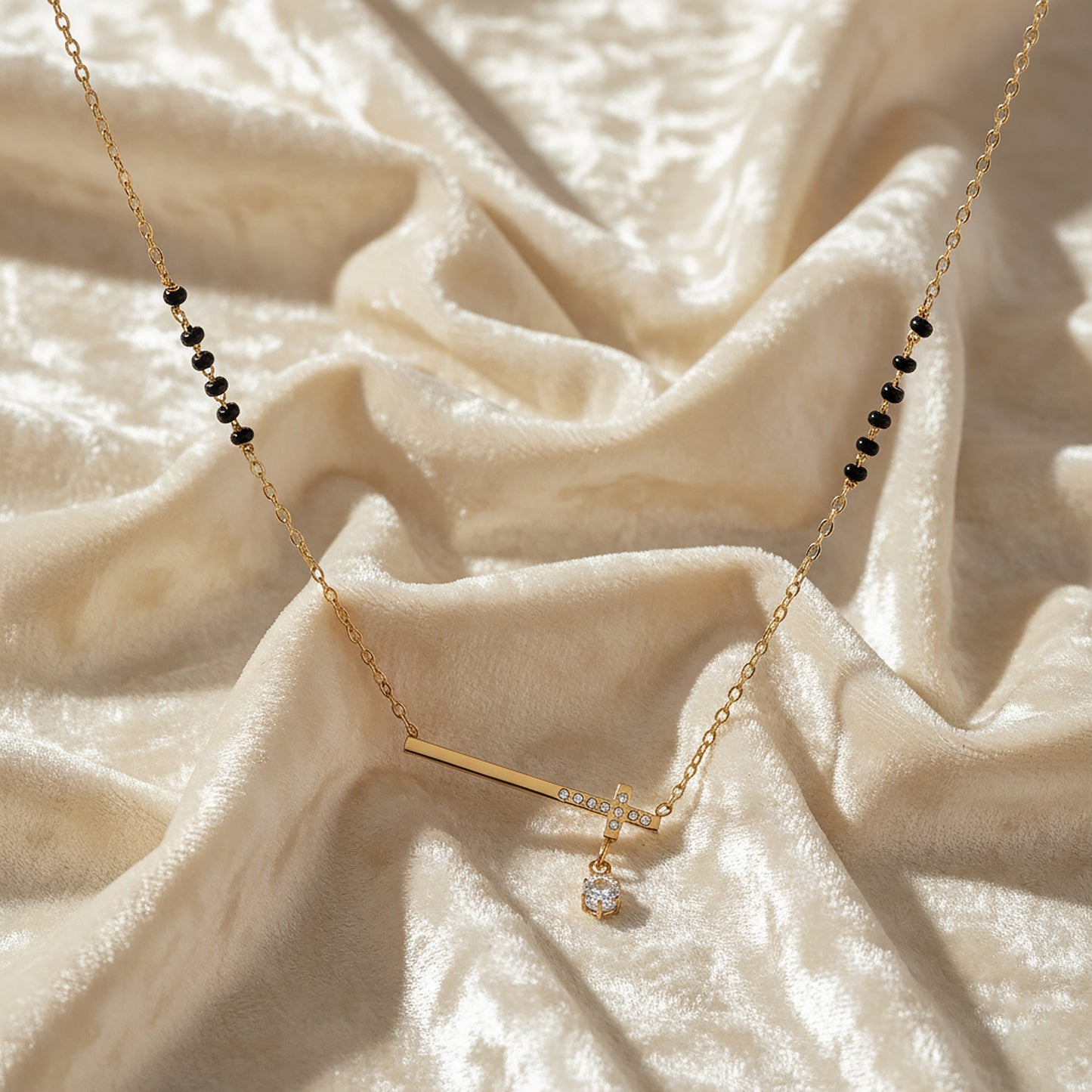 Black beads gold mangalsutra with minimal bar pendant and solitaire drop displayed on cream velvet fabric