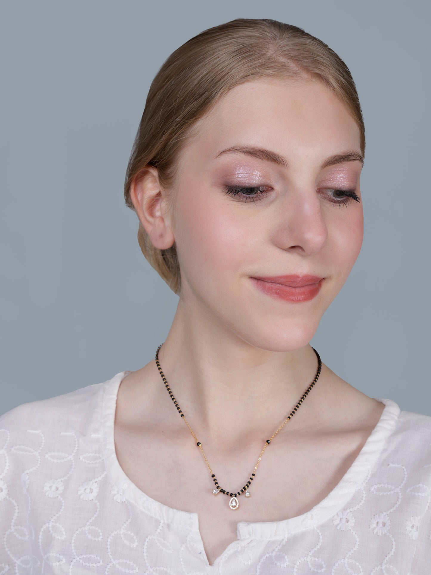 Minimalist mangalsutra pendant design on a gold chain, featuring a central cluster of black beads and a sparkling teardrop drop, modeled on a woman