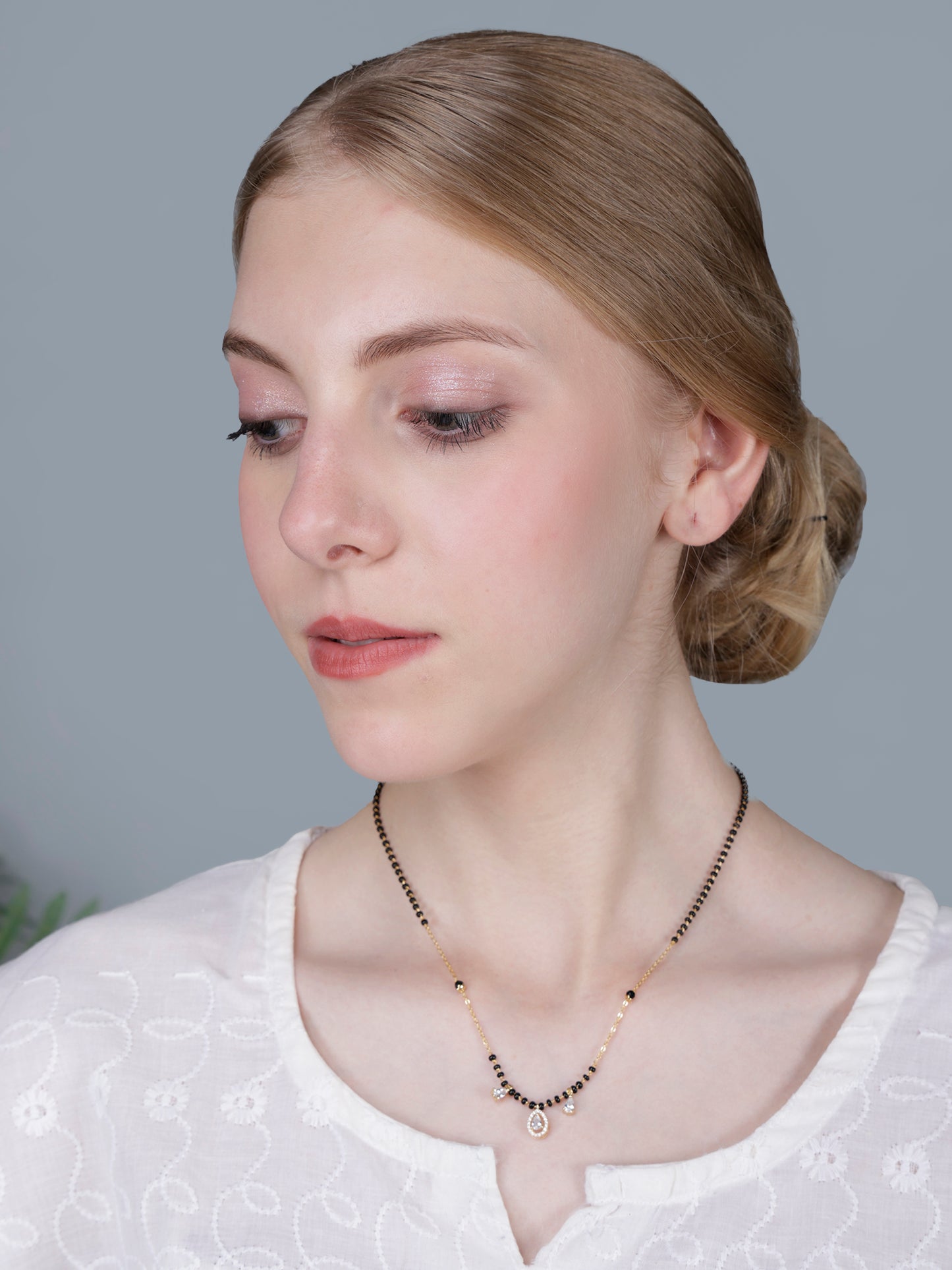 Simple modern mangalsutra design featuring a delicate gold chain with black beads and teardrop pendant, modeled on a woman.