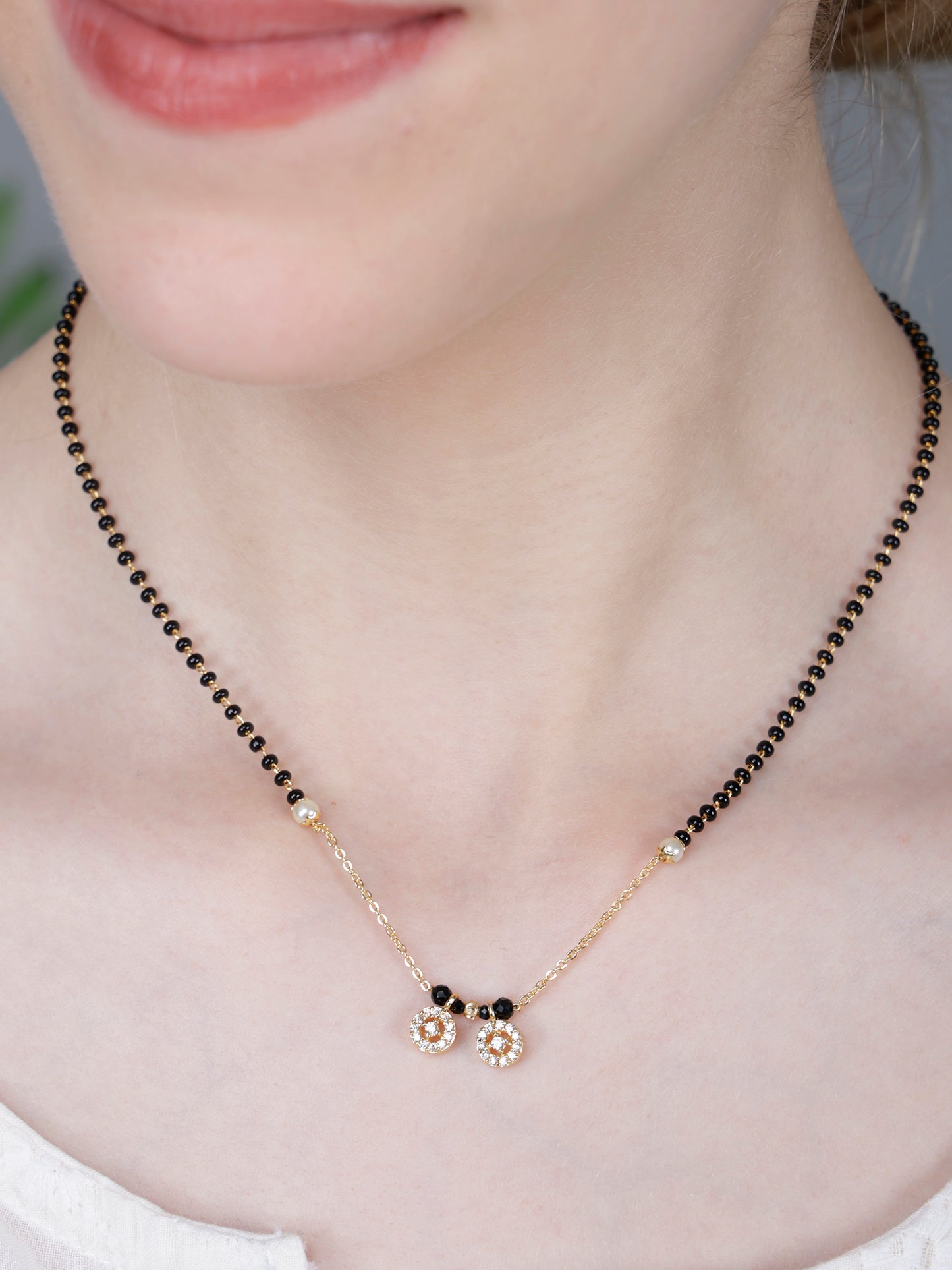 Mangalsutra Design with black beads and gold chain. Features two small, round, floral-inspired pendants studded 