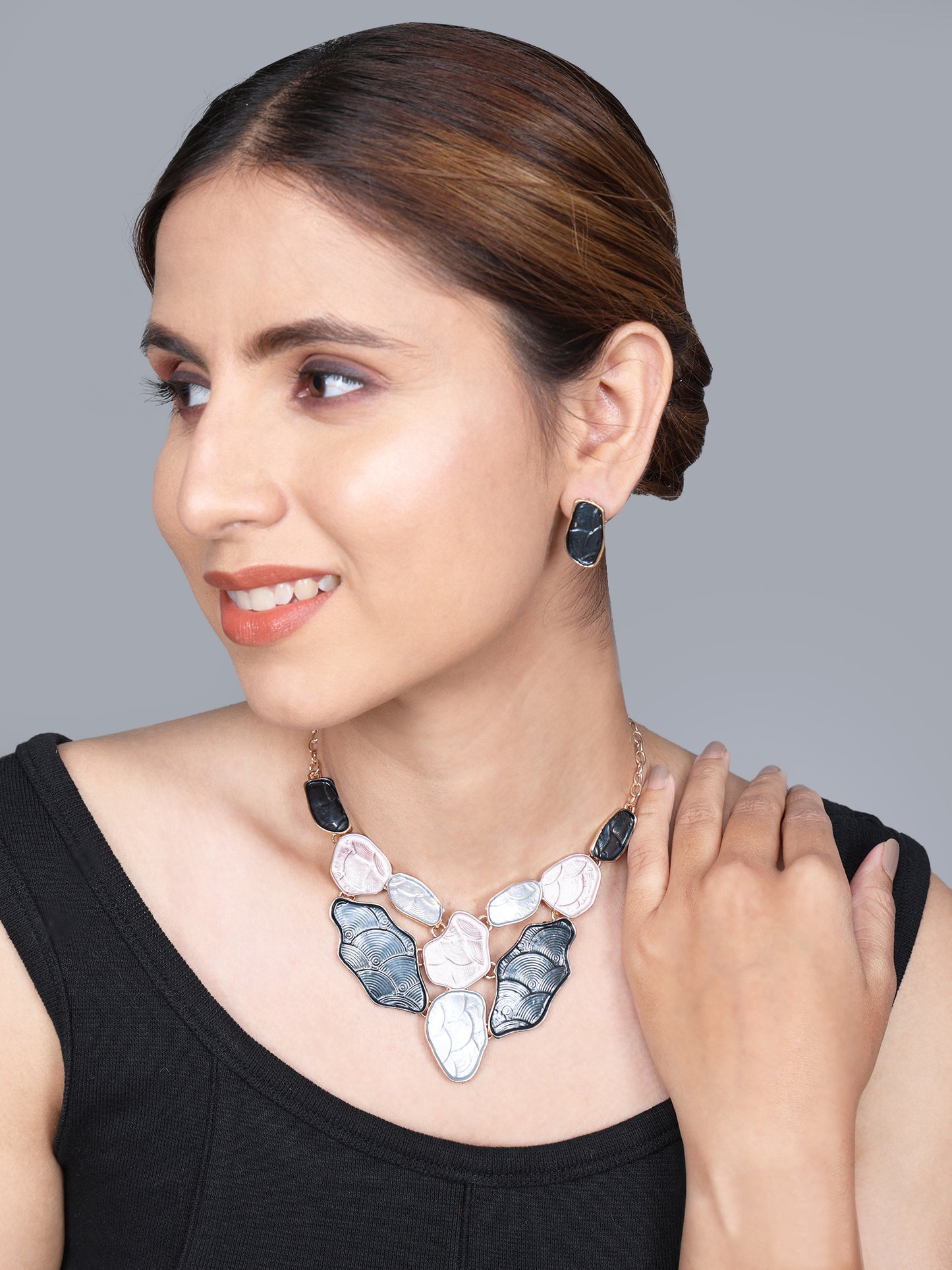 A woman wearing a modern gold choker necklace with black and cream abstract stones, paired with matching studs.
