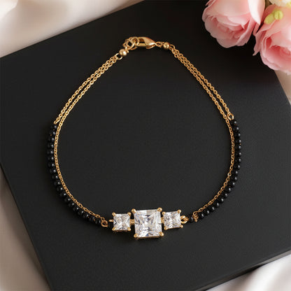 Modern mangalsutra design bracelet with black beads and three sparkling square stones, displayed on a black box with pink roses beside it.