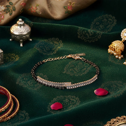 Modern mangalsutra design bracelet with black beads and sparkling stones on green fabric.