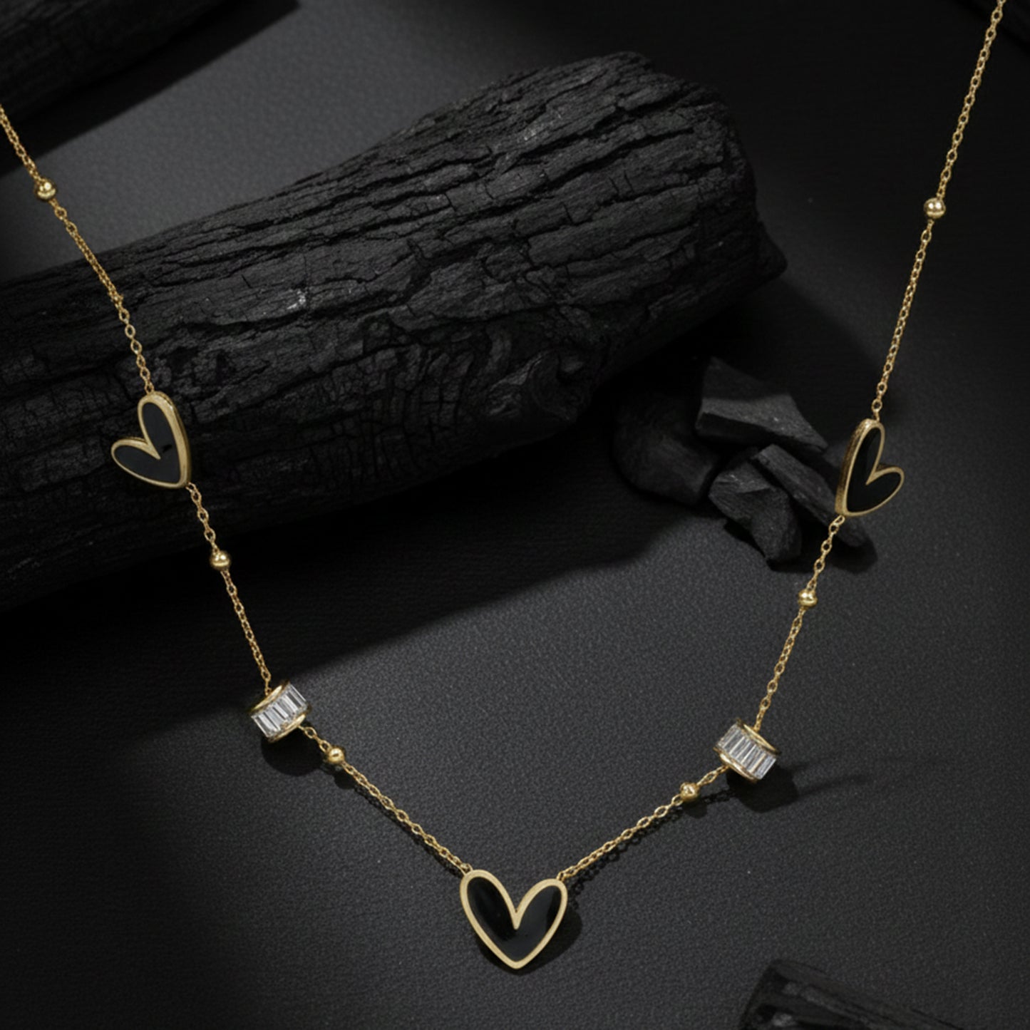 Necklace pendant designs gold finish with black heart motifs displayed on a textured charcoal background.