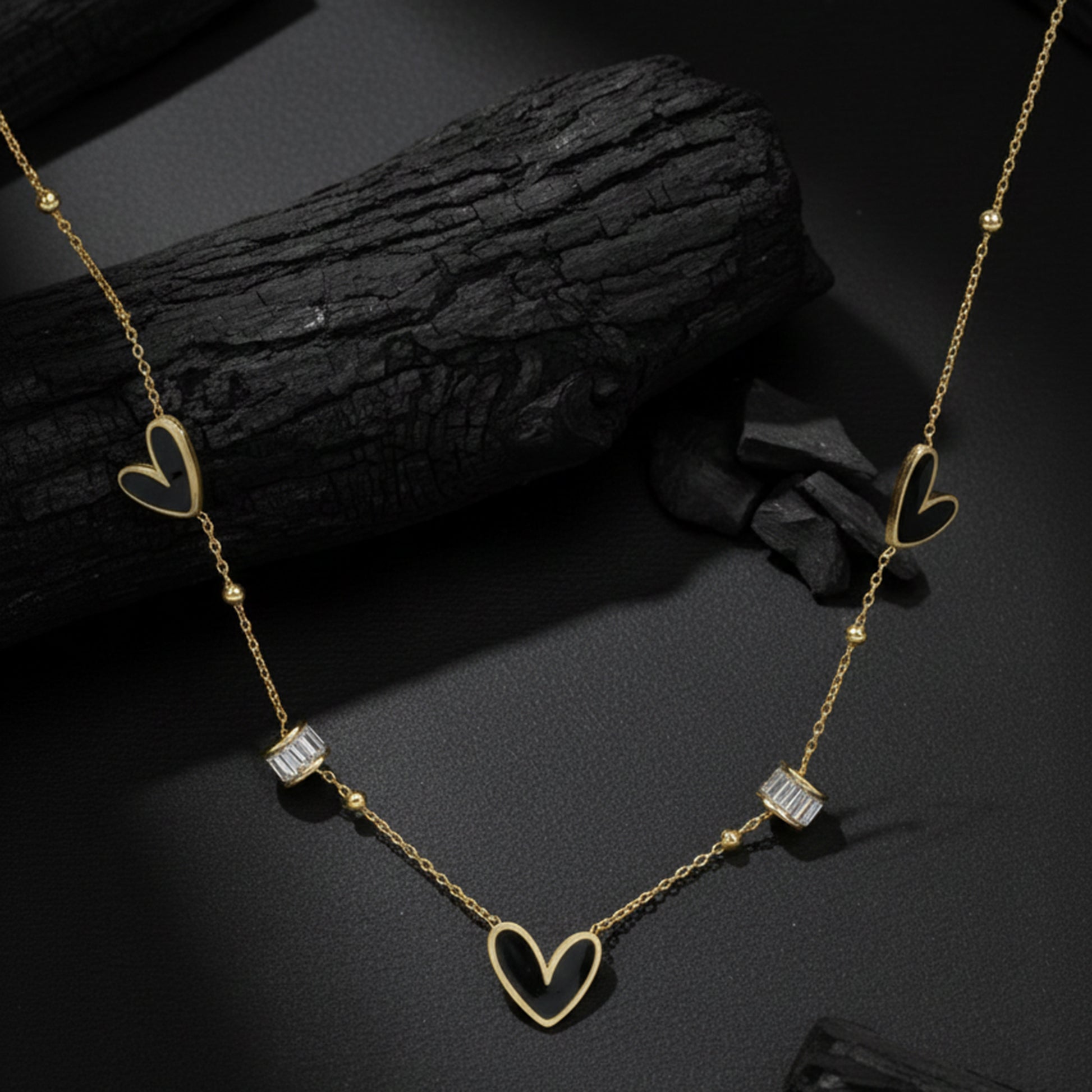 Necklace pendant designs gold finish with black heart motifs displayed on a textured charcoal background.