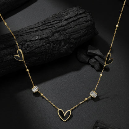 Necklace pendant designs gold finish with black heart motifs displayed on a textured charcoal background.