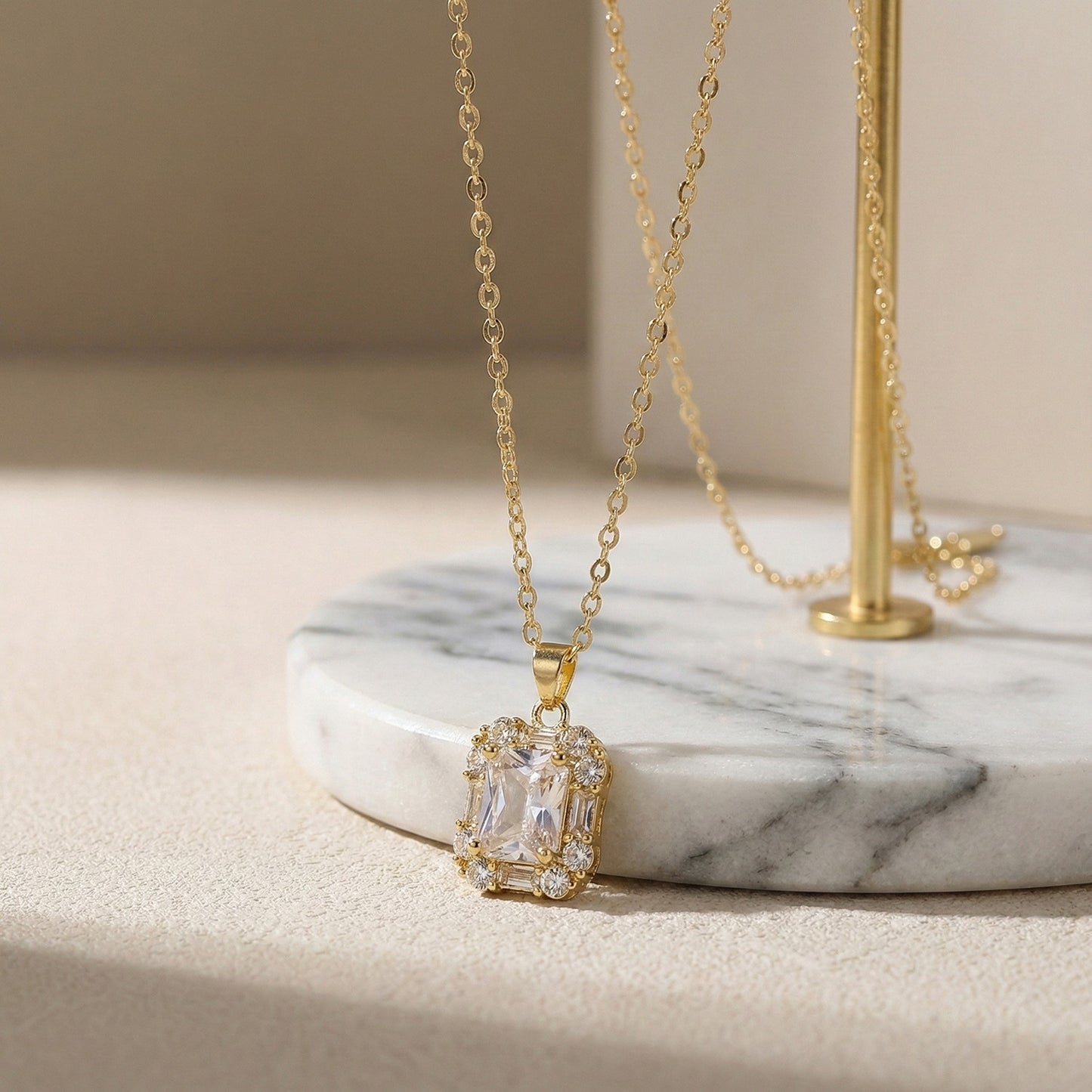 Elegant necklace pendant designs in gold with a brilliant-cut center stone, resting on a white marble display.