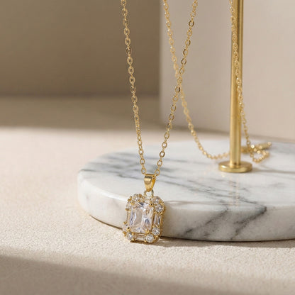 Elegant necklace pendant designs in gold with a brilliant-cut center stone, resting on a white marble display.