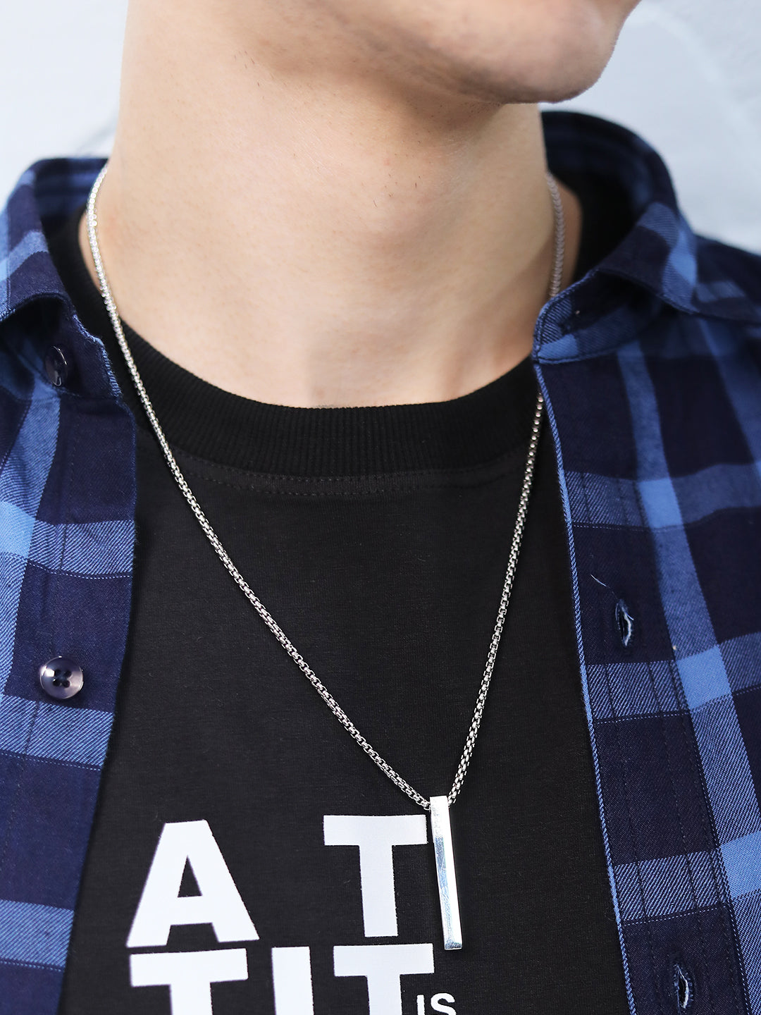 Men silver necklace and pendant worn with a casual T-shirt and check shirt.