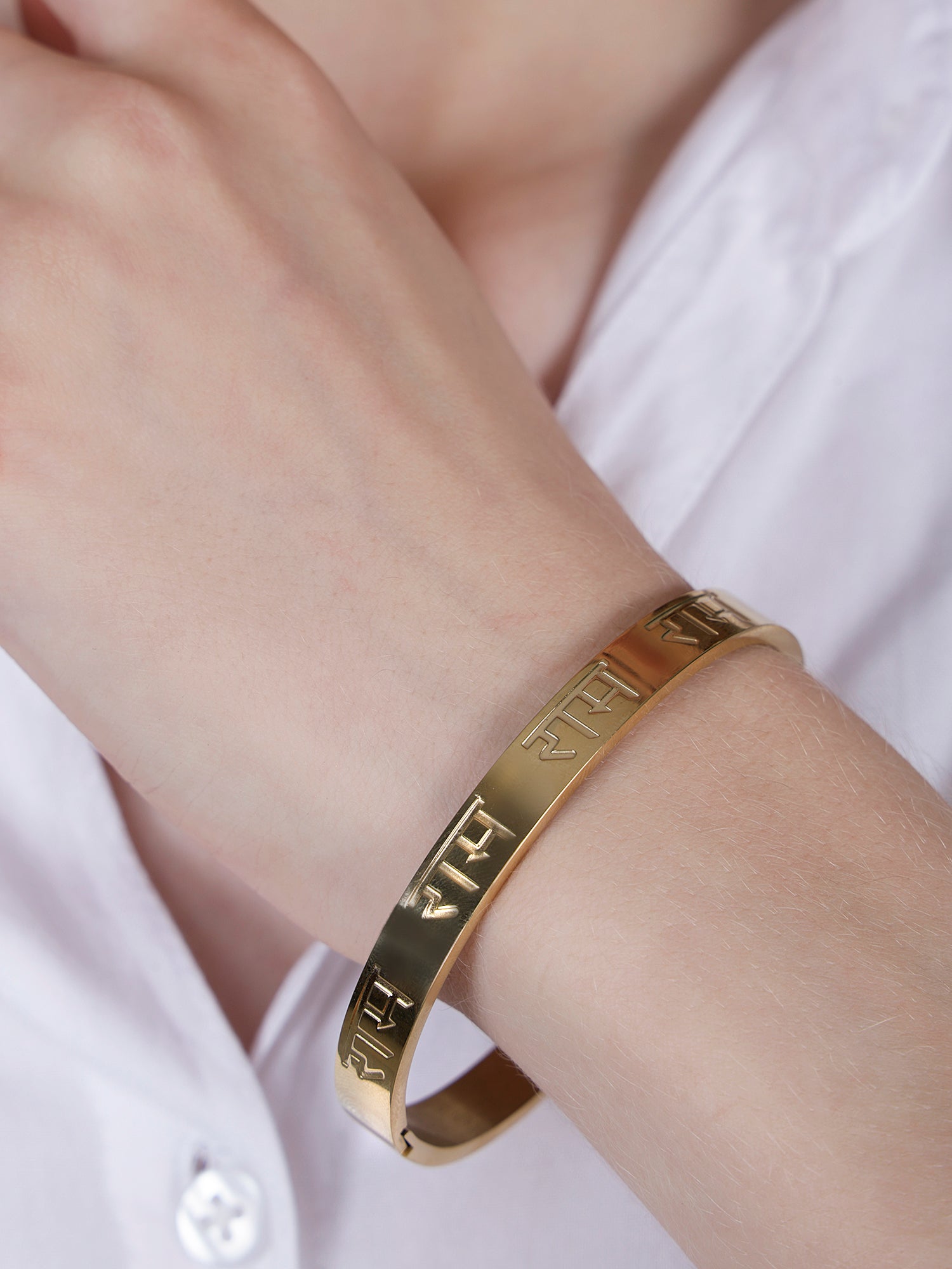 Close up shot of a stylish gold bracelet design for women worn on a wrist with a white shirt.