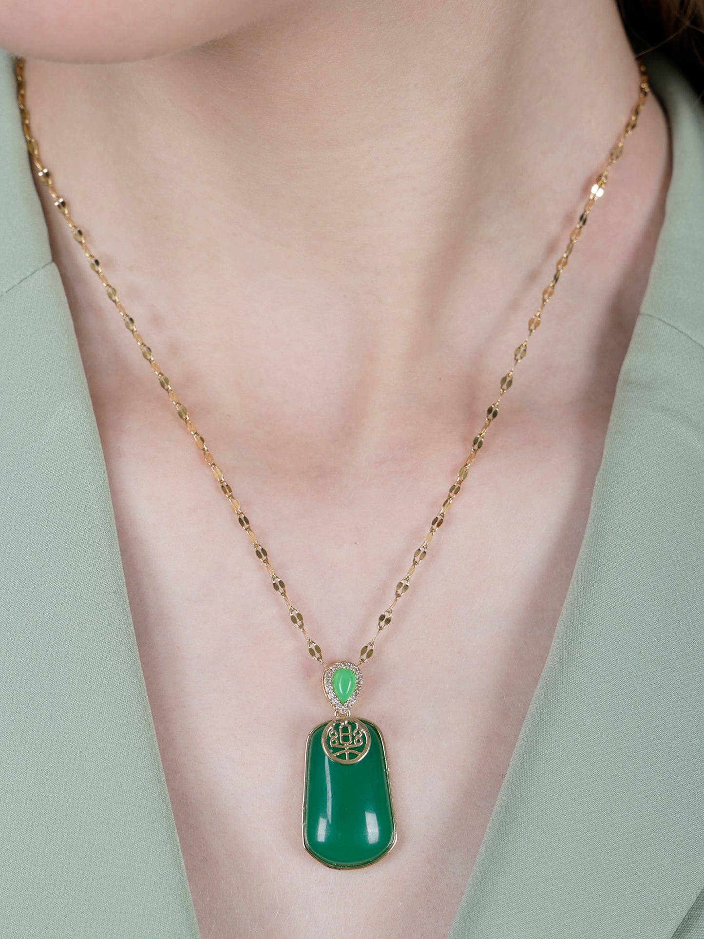 Close-up of modern gold necklace designs for women, showcasing a polished green stone pendant against a pale green blazer
