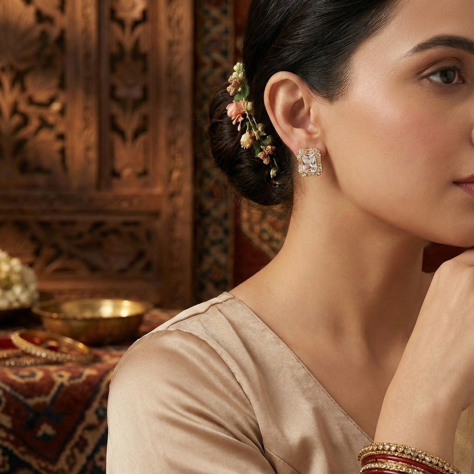 Detailed view of a small gold earring from a matching jewelry set, worn by a model with an elegant updo.