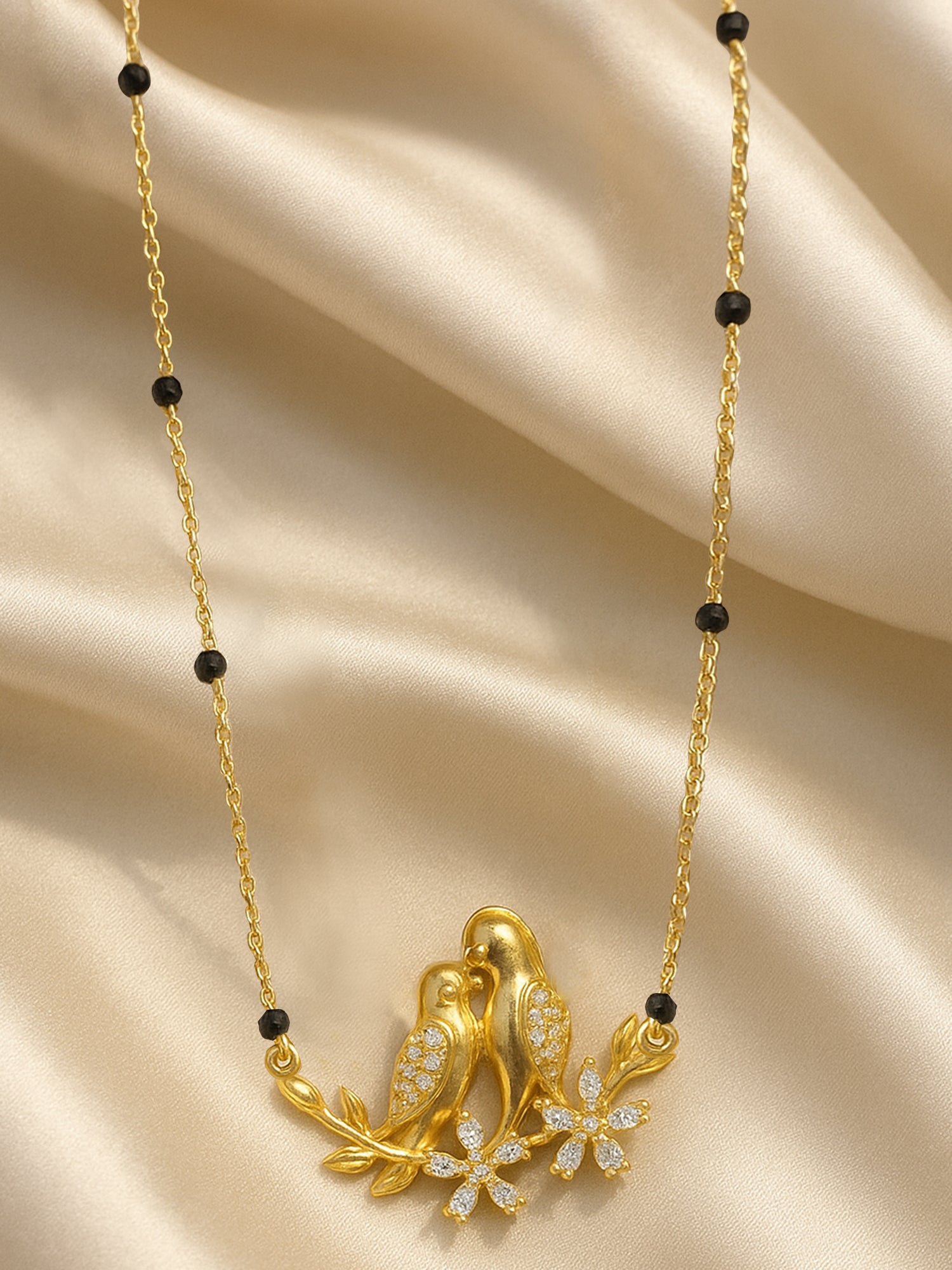 Contemporary gold mangalsutra pendant with an intricate bird motif and sparkling diamond-cut stones, set on a smooth, golden fabric
